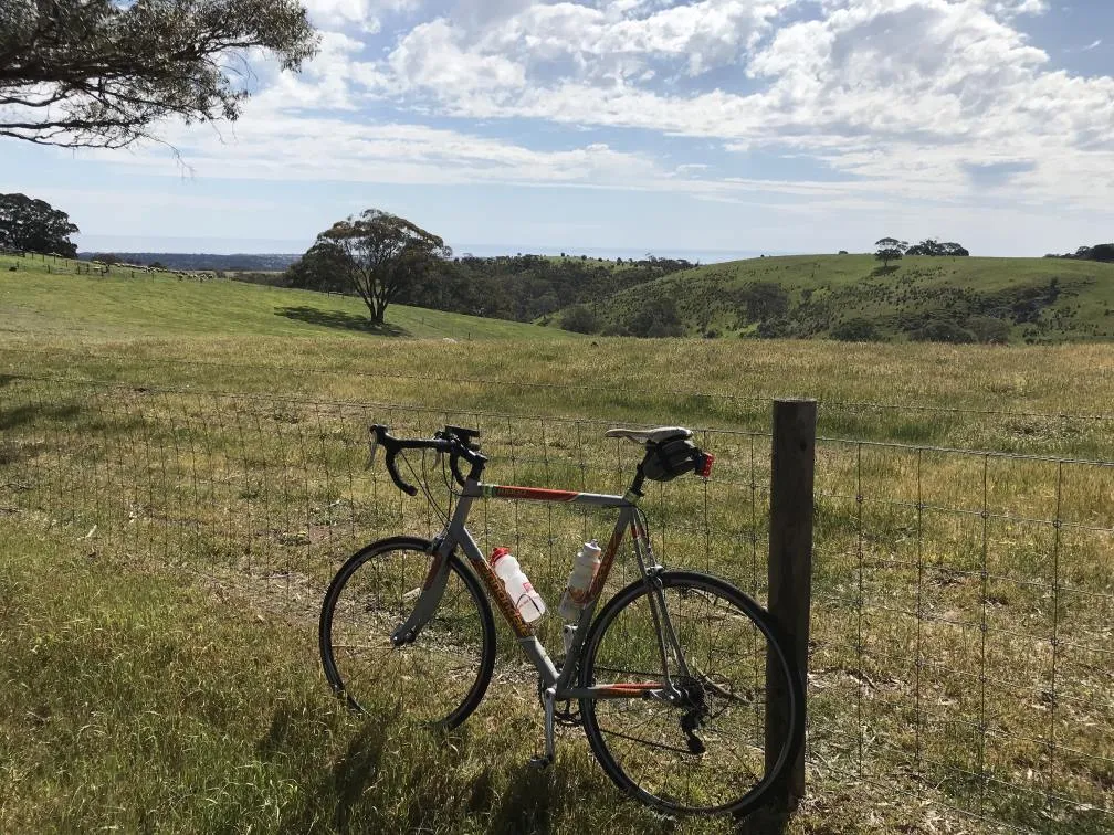Bicycle sitting next to a fence, overlooking green rolling hills