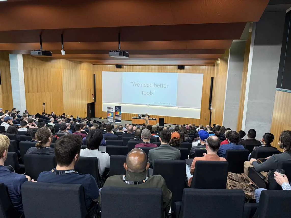 View of main auditorium from the back. Lots of people seated listing to keynote