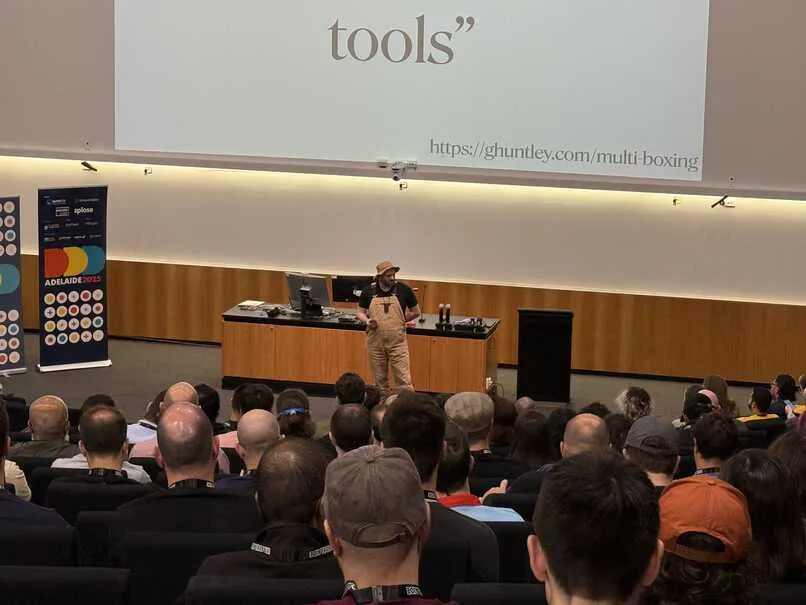 Geoffrey presenting keynote, dressed in overalls and wearing a straw hat