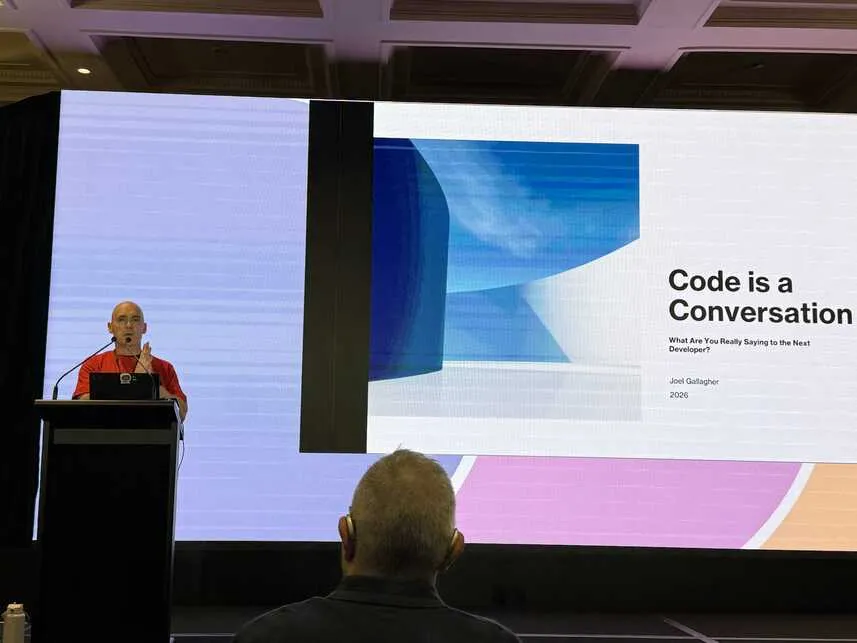 Joel standing behind lectern with title slide behind him