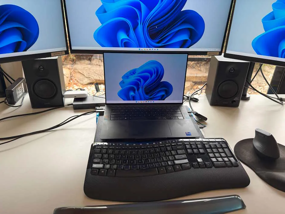 Speakers on David's desk, with laptop and three monitors