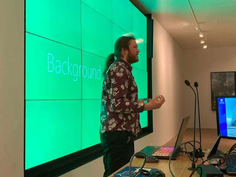 Multi-screen display with Ryan presenting in front of it