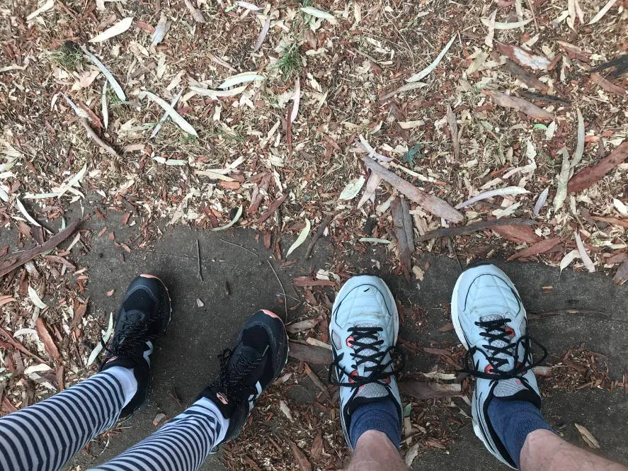 Two pairs of legs, with concrete path and grass with leaves