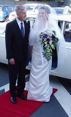 Fiona in a white wedding dress getting out of a car with her father